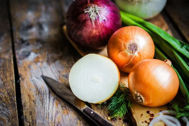 Červená, žlutá a zelená cibule s nůžkou na dřevěném povrchu.