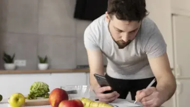 Muž počítá kalorie pomocí telefonu a poznámek v kuchyni