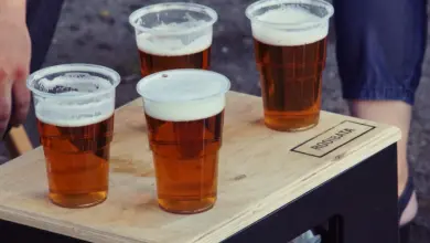 Čtyři plastové šálky s pivem na dřevěném paletu.
