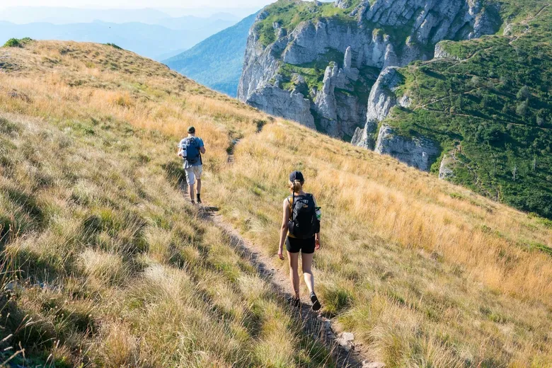 Dva turisté jdou po lesní cestě v horách.