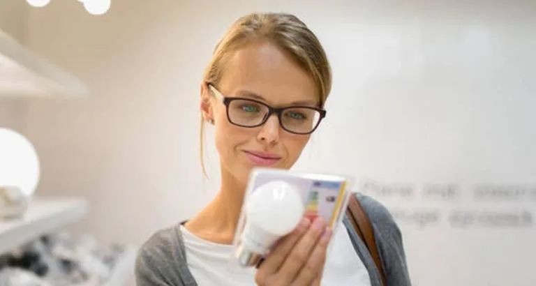 Žena drží balení žárovky v obchodě pro osvětlení.