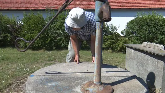 Muž zkoumá starý vodní studen s ručním čerpadlem venku.