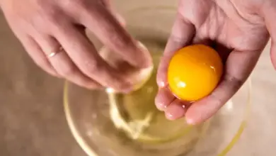 Ruce oddávají žloutek z prasklého vejce do skleněné misky.