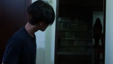 Muž se dívá na stínovou postavu v temné místnosti.