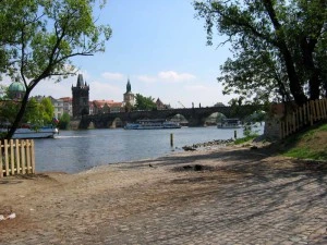 Pohled na řeku Vltavu v Praze s mostem a historickými budovami.