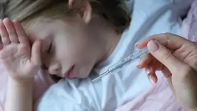 Dítě leží v posteli s teploměrem u ruky dospělé osoby.