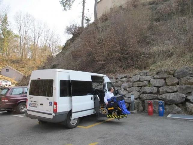 Bílý přístupový vůz na parkovacím místě pro invalidy s rozloženou rampou.