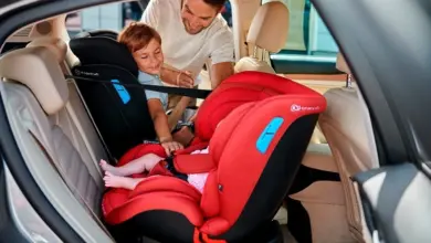 Muž pomáhá dítěti sedět v červeném autosedačce pro kojence.