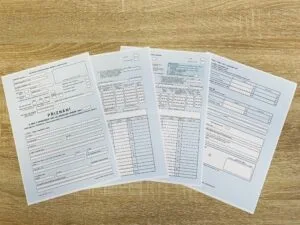 Čtyři formuláře s tabulkami rozložené na dřevěném stole.