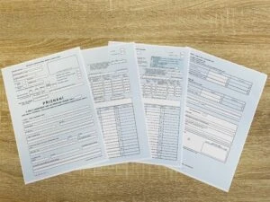 Čtyři papírové formuláře s finančními údaji na dřevěném stole.