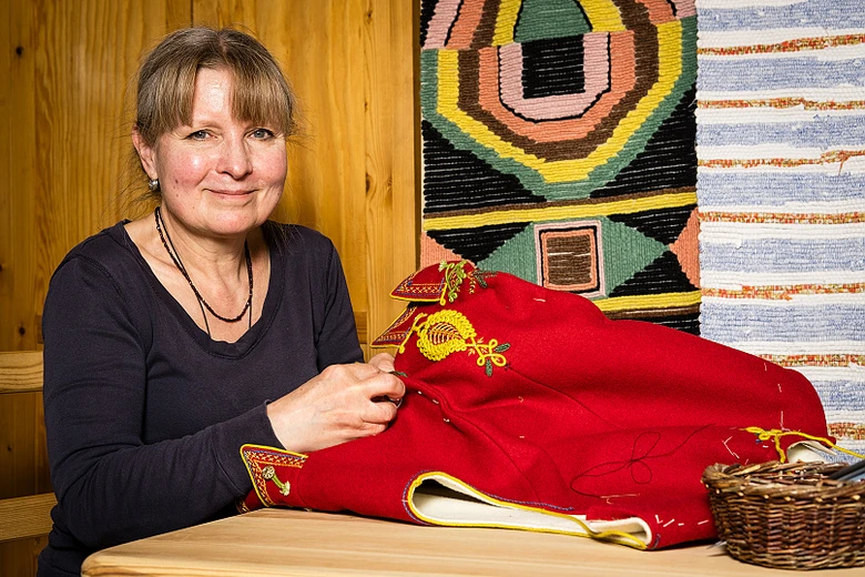 Žena šije červený valašský kroj s žlutou výší