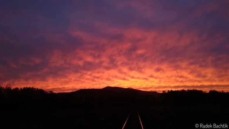 Západ slunce s červenými mraky nad tmavým horizontem.