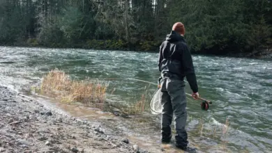Muž chytá ryby v řece s letovým prutem.