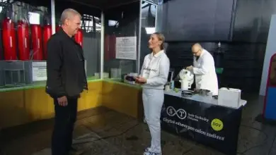 Tři lidé u stolu s výukovou demonstrací v průmyslovém prostoru.