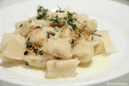 Gnocchi s bylinkami a sýrem na bílém talíři.