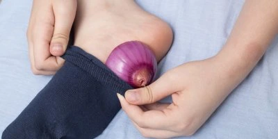 Cibule v modré ponožce na chodidle pro nachlazení.