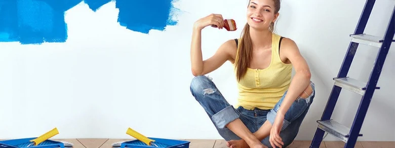 Žena maluje bílou zeď sytou modrou barvou s válečkem.