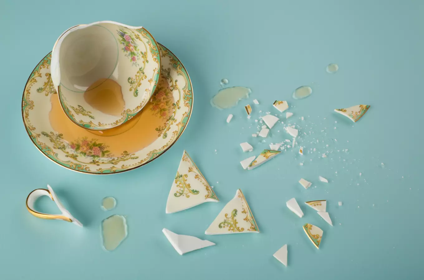 Rozbitý porcelánový šálek s tekutinou na modrém pozadí.