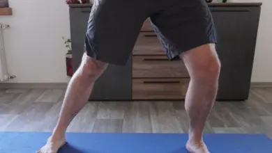 Muž stojí na modré podložce s rukama v pase.