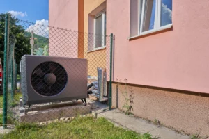 Venkovní jednotka tepelného čerpadla u domu pro ohřev vody.