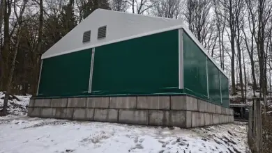 Zelená přechodná budova stojí na sněhu v lesu.