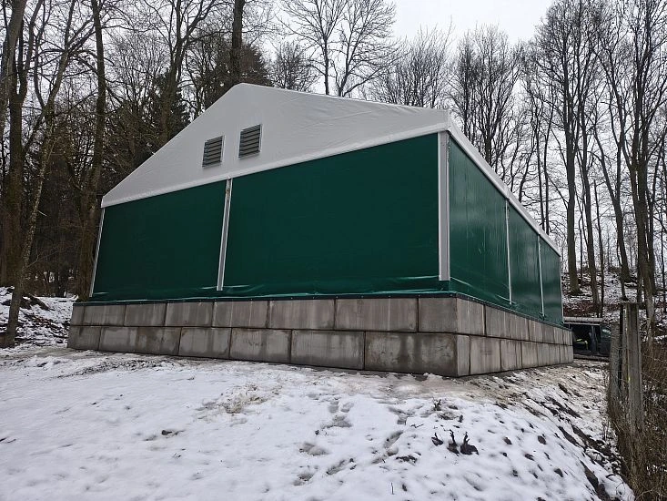 Zelená přechodná budova stojí na sněhu v lesu.