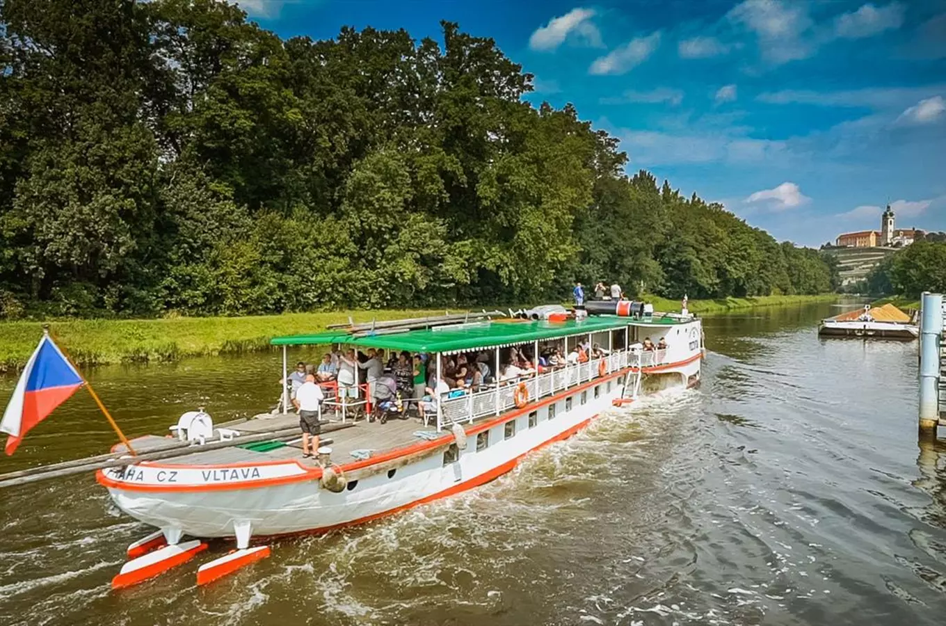 Turistická loď pluje po řece s pasáži pod zelenou střechou.