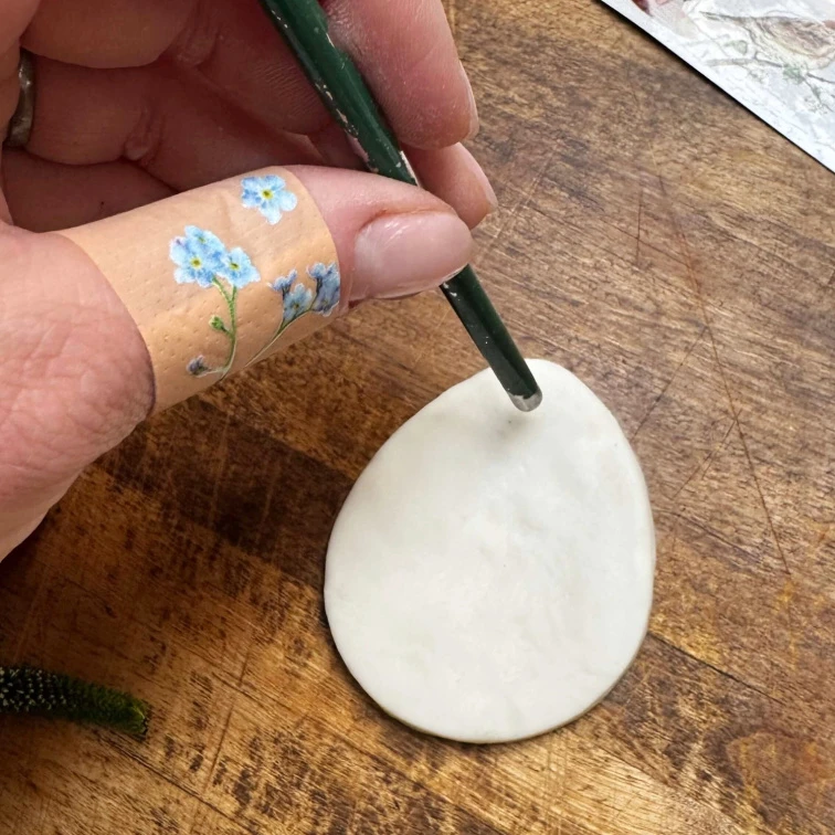 Ruka s náramkem maluje bílý disk z chladného porcelánu.