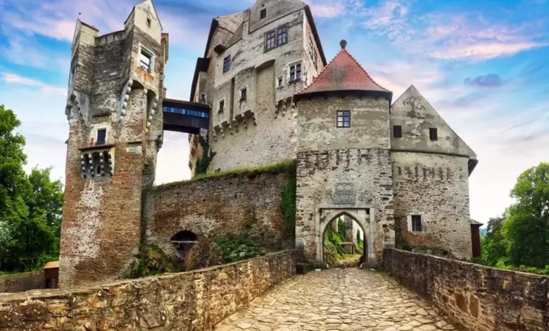 Starý kamenný hrad s věžemi a bránou na pozadí modré oblohy.