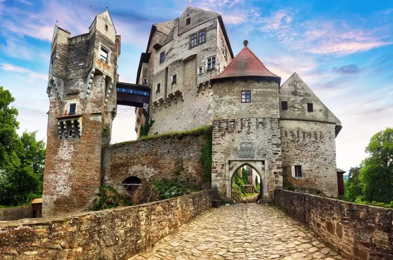 Starý kamenný hrad s věžemi a bránou na pozadí modré oblohy.